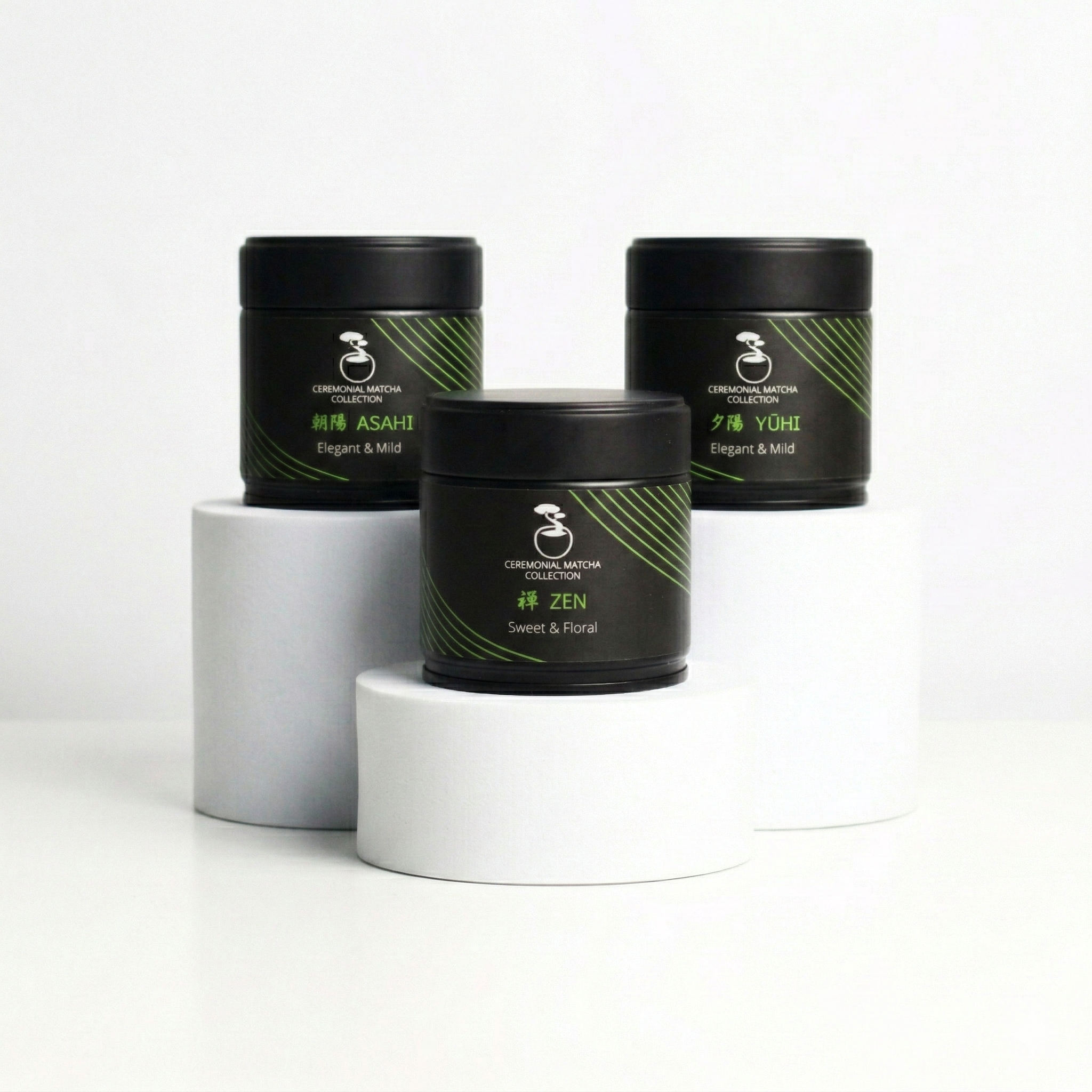 Three black tins of Bonsai Matcha Ceremonial Collection, featuring Asahi, Zen, and Yuhi blends, displayed on minimal white pedestals against a clean white background
